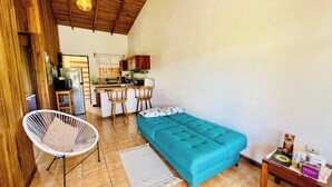 A compact room with a teal sofa, a white chair, a small table with items, and a kitchen area with a refrigerator and cabinets. - Cozy & Beautiful Casa Aire, Near Lake Park & Town (Arenal)
