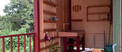 A covered balcony with a wooden ceiling, a table, two wicker chairs, and a potted plant.