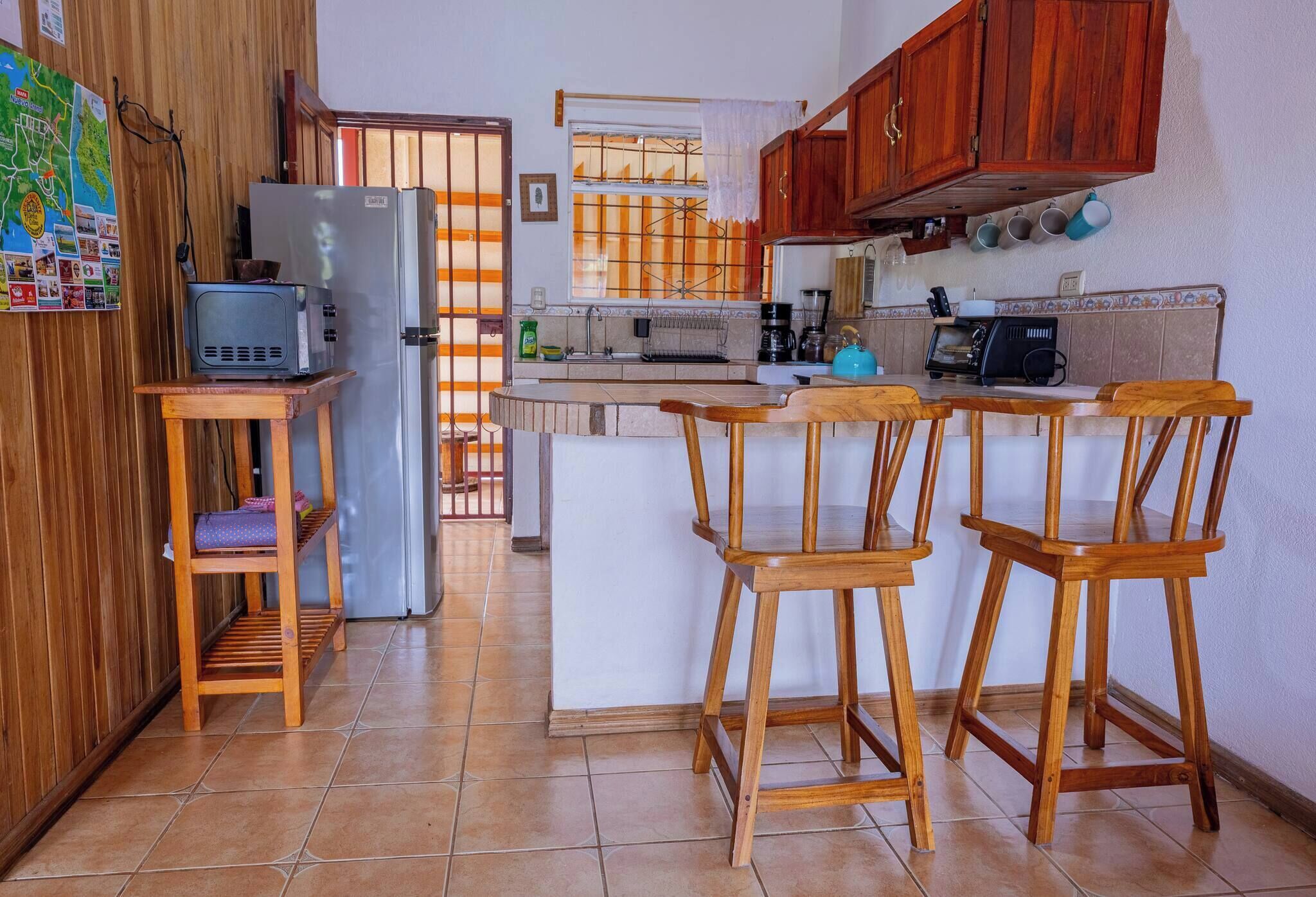 Eine kompakte Küche mit Kühlschrank, Mikrowelle und Kaffeemaschine. Holzstühle und ein kleiner Tisch sind vorhanden.
