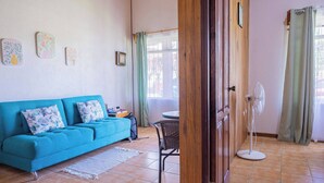 A living room with a teal sofa, patterned cushions, a small table, and a fan. - Cozy & Beautiful Casa Aire, Near Lake Park & Town (Arenal)