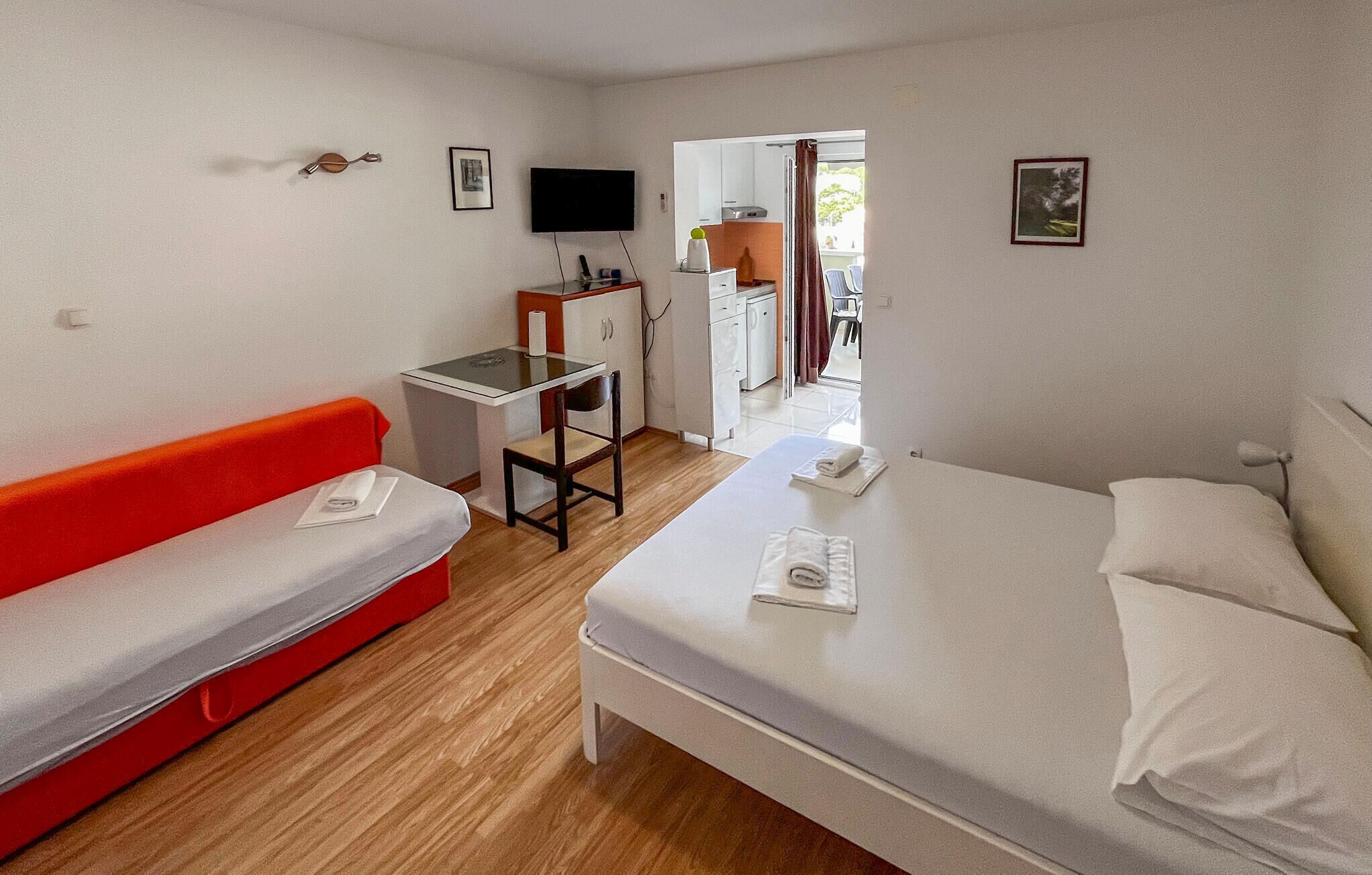 A hotel room with a bed, a desk with a chair, a red sofa, and a TV on the wall.