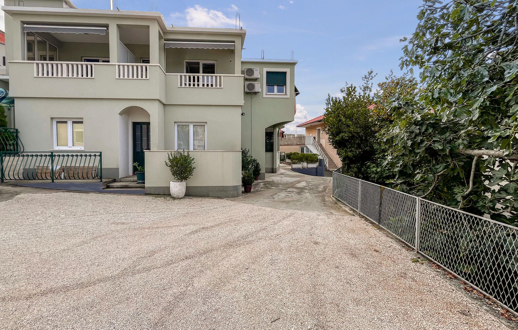 A two-story building with balconies, a gravel driveway, and a metal fence.