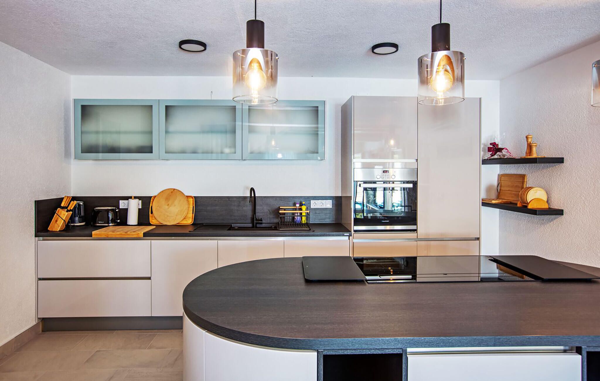 Een moderne keuken met een gebogen eiland, roestvrijstalen apparatuur en glazen kasten.