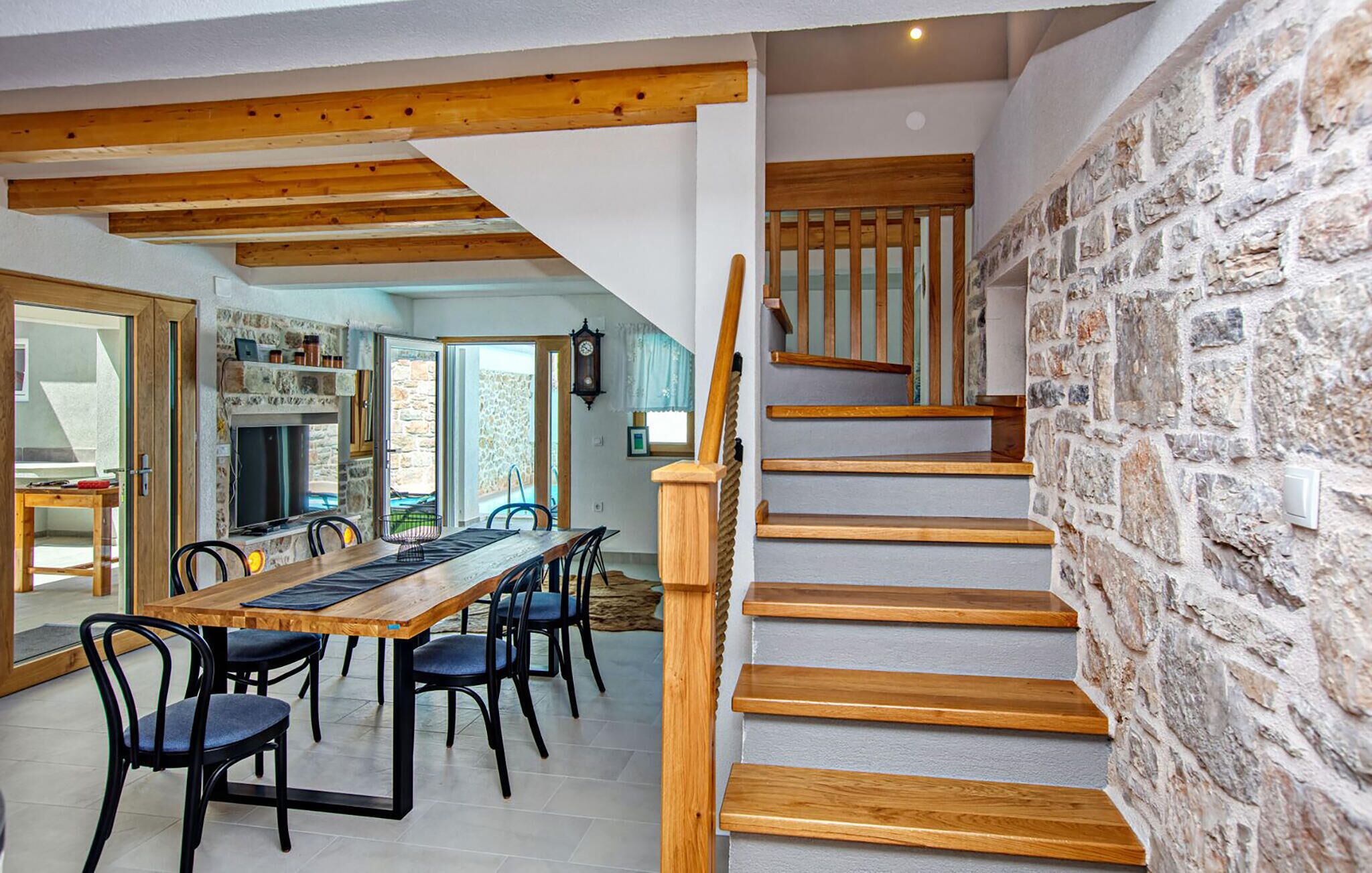A dining area with a wooden table and chairs, a stone wall, and a staircase with wooden steps and a wooden handrail.