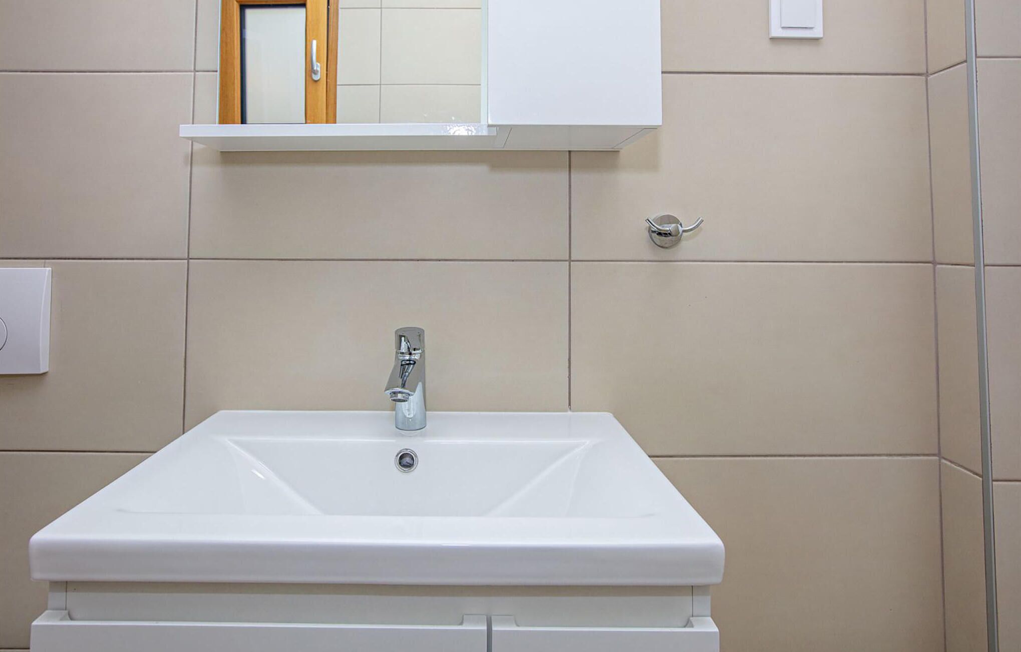 Een badkamer met een wit wastafelmeubel, een spiegel erboven en beige betegelde wanden.
