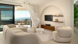 A modern living room with a large window, comfortable seating, a flat-screen TV, and a minimalist decor.