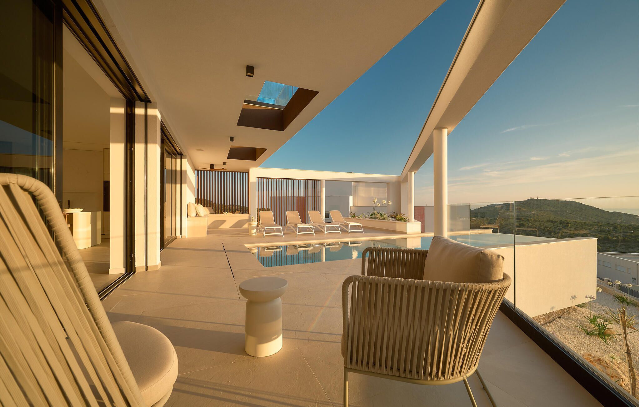 Un espace de détente extérieur moderne, doté d’une piscine, de sièges et offrant une vue sur le paysage.