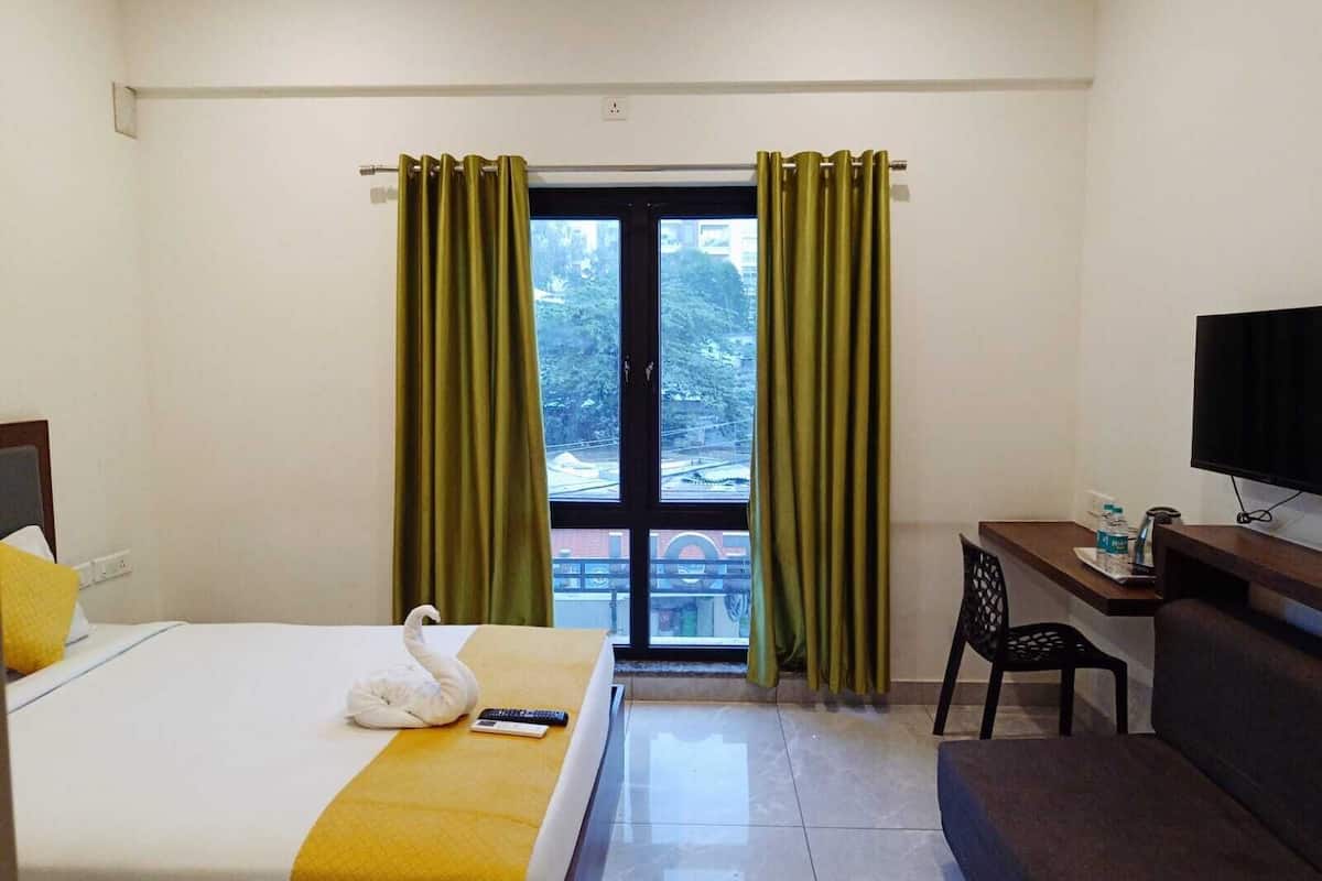 A hotel room with a bed, a desk, a chair, a TV, and a window with curtains.
