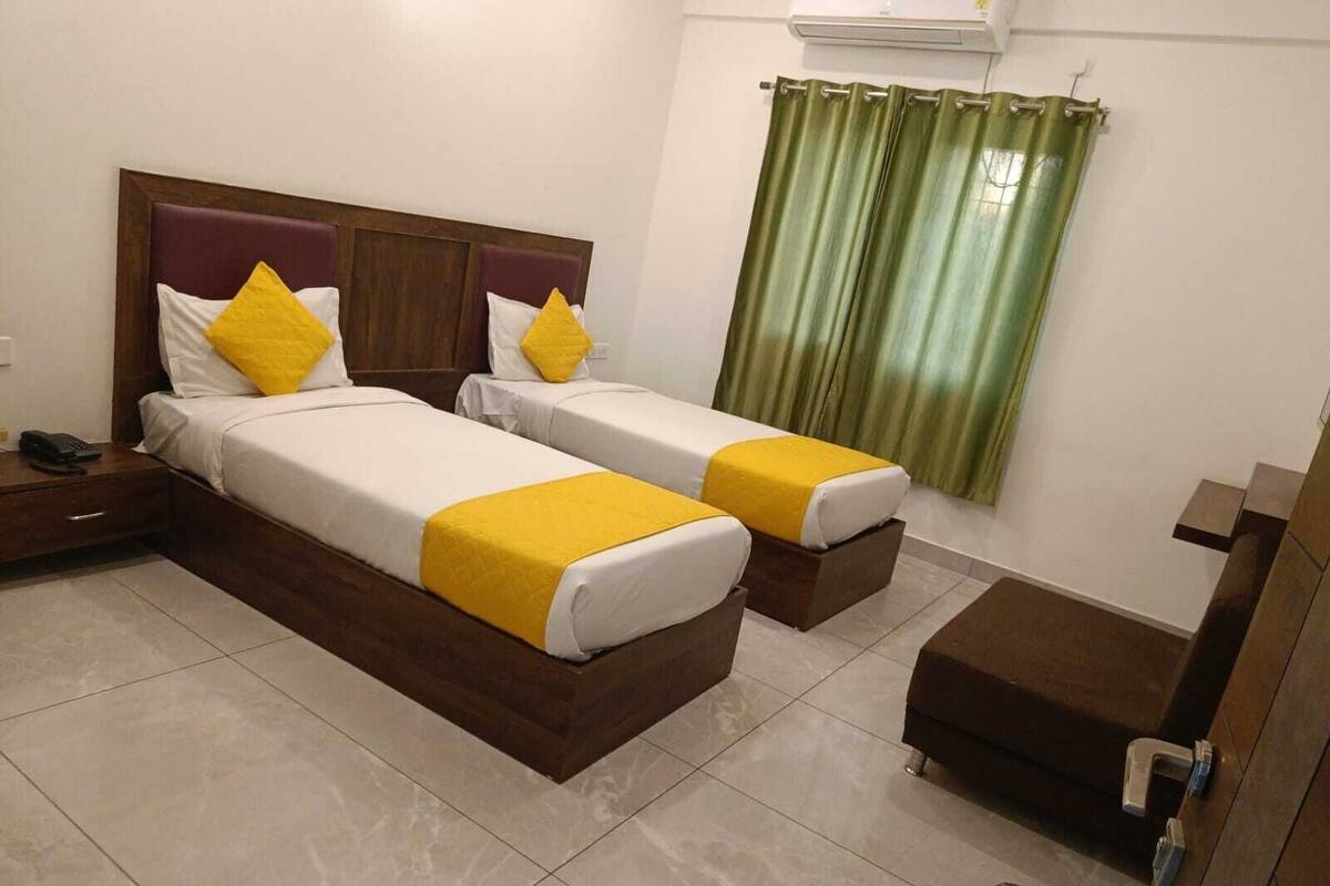 A hotel room with two beds, a nightstand, a desk, and a green curtain.