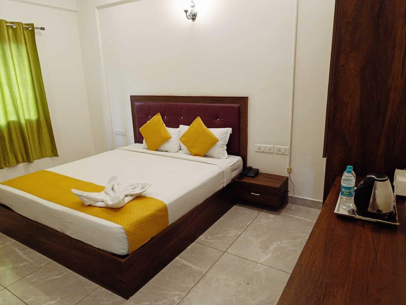 A hotel room with a bed, a bedside table, a nightstand, a lamp, a water bottle, and a coffee maker.
