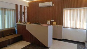 Ένας χώρος υποδοχής με έναν τοίχο επενδυμένο με ξύλινα πάνελ, έναν πάγκο υποδοχής, έναν ανεμιστήρα οροφής και ένα παράθυρο με περσίδες.