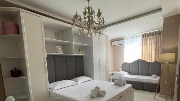 A modern bedroom with a bed, a wardrobe, a desk, and a chandelier. - Edion Center Apartment (Shkodër)