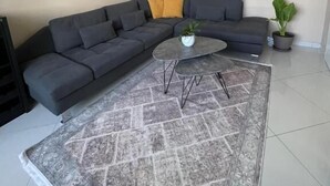 A modern living room with a grey sectional sofa, a small coffee table, and a patterned rug. - Edion Center Apartment (Shkodër)
