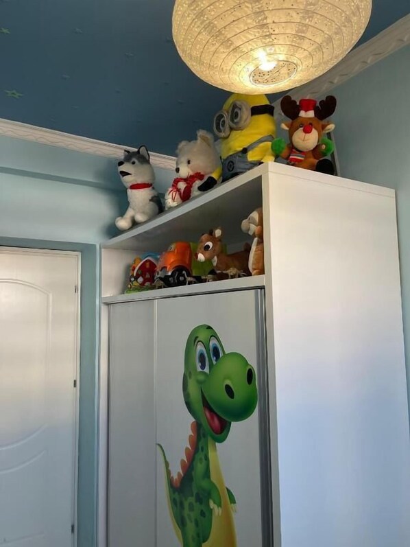 A room with a white wardrobe, a dinosaur mural, and various stuffed toys on shelves. - Edion Center Apartment (Shkodër)