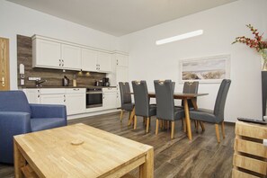 A modern kitchen with white cabinets, a dining area with a wooden table and grey chairs, and a blue sofa.