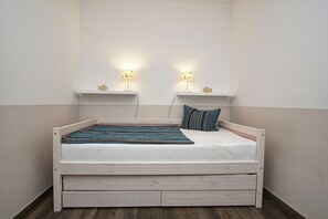 A single bed with a wooden frame, a white mattress, and a blue and brown striped blanket. There are two wall-mounted lamps with fish-shaped lights on either side of the bed. - Free use of the AHOI adventure pool and sauna - Kurhaus Nordstrand FeWo 31 - (Baabe)