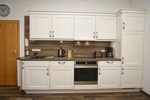 A kitchen with white cabinets, a wooden countertop, a coffee maker, and a kettle.
