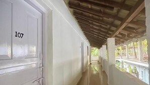 Un couloir avec une porte blanche portant le numéro 107, des poutres en bois au plafond et une vue sur la verdure à l’extérieur.