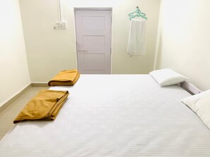 A hotel room with a bed, two folded towels, a white door, and a wall-mounted towel rack. - Palolem Paradise Guest House (Canacona)