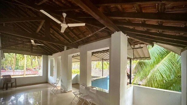 Une pièce spacieuse avec un plafond haut, un ventilateur de plafond et de grandes fenêtres donnant sur des palmiers et une piscine.