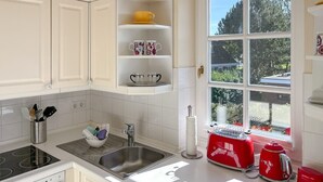 Una cocina moderna con armarios blancos, un lavamanos de acero inoxidable, una estufa a gas y un ventanal con vistas a zonas verdes.