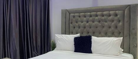 A bedroom with a tufted headboard, a large bed with white bedding, and a dark curtain.