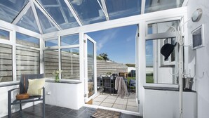 A conservatory with a bench, a wicker basket, and a view of the garden outside. - Little Tresevens is a generously sized detached home (Polzeath)