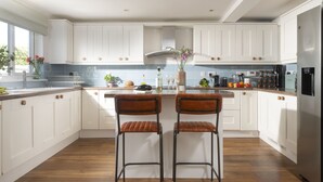 A modern kitchen with white cabinets, a stainless steel refrigerator, and two bar stools. - Little Tresevens is a generously sized detached home (Polzeath)