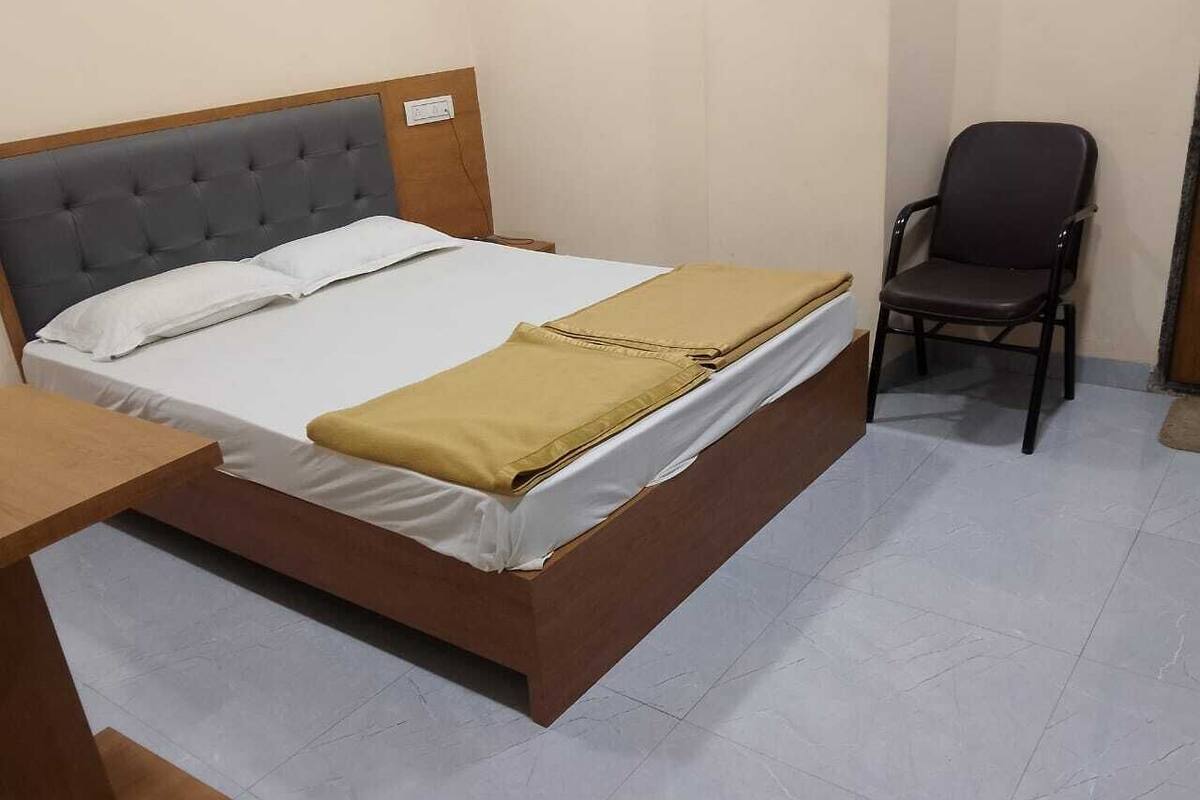 Ein Einzelbett mit Holzrahmen und Kopfteil, ein kleiner Holztisch und ein schwarzer Bürostuhl in einem Raum mit Fliesenboden.