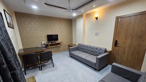 Una sala de estar con un sofá, un televisor sobre un mueble bajo, una mesa de comedor con sillas y una puerta de madera.