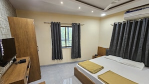 Habitación de hotel con cama, televisor, armario de madera, ventana con cortinas y equipo de aire acondicionado.