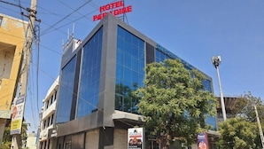 Un edificio moderno de hotel con una amplia fachada de vidrio, un llamativo letrero 'HOTEL PARADISE' y un letrero 'SUNSHINE' que indica un restaurante.