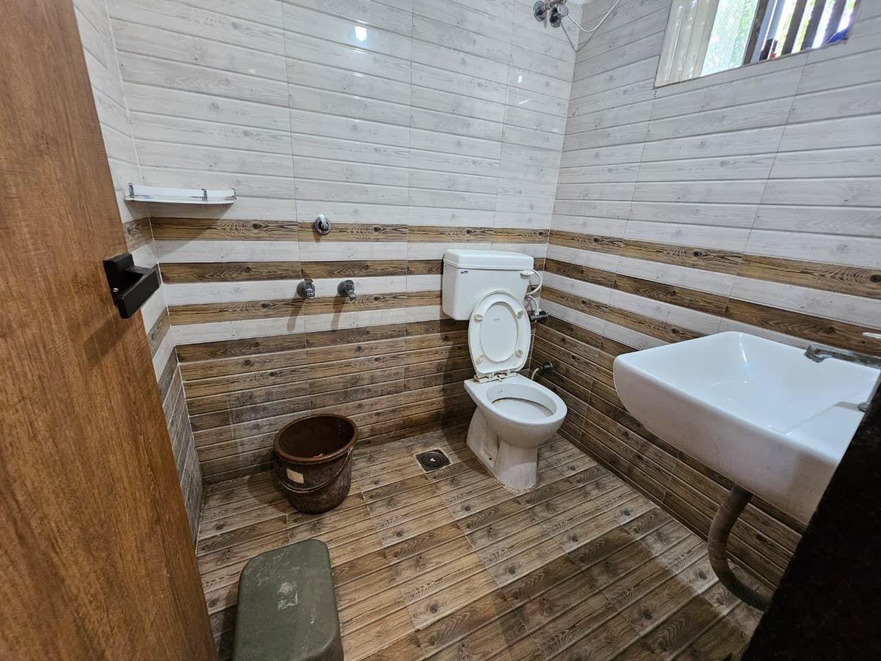 Et badeværelse med trægulv, toilet, vask og bruseniche.