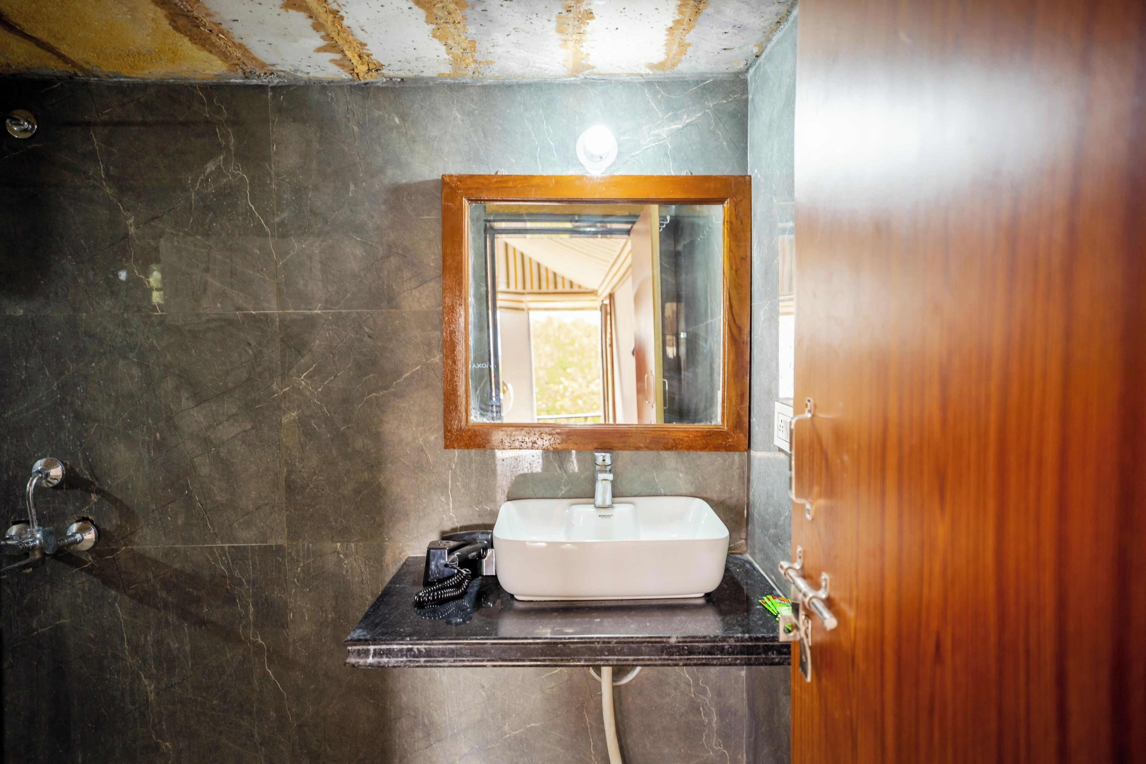 A bathroom with a marble sink, a wooden-framed mirror, and a shower with a visible pipe.