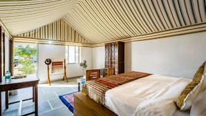 Un dormitorio con techo inclinado, una cama, un escritorio, una silla, un ventilador y una estantería.