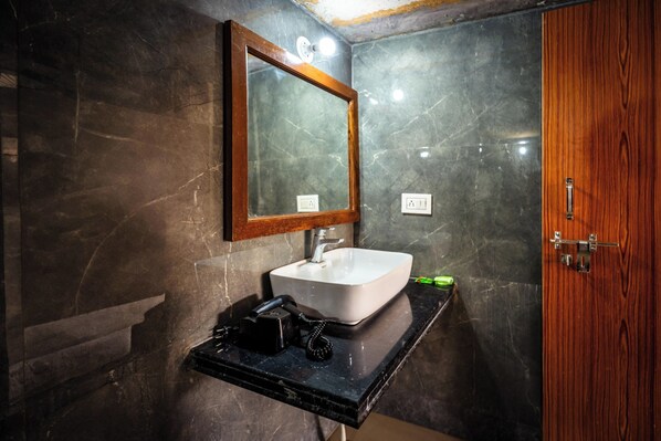 A bathroom with a marble wall, a wooden door, a sink with a mirror, and a black countertop. - The Saffron Desert Camp (Sam)