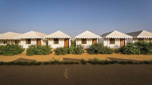 Una hilera de tiendas blancas con puertas y ventanas de madera, ubicadas en un paisaje desértico con poca vegetación.