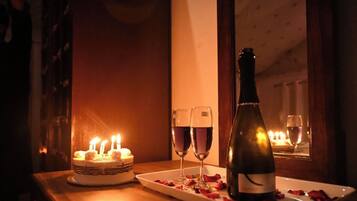 Uma mesa com bolo, duas taças de vinho, uma garrafa de vinho e pétalas de rosa.