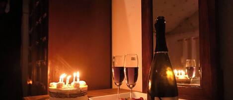A table with a cake, two glasses of wine, a bottle of wine, and rose petals.