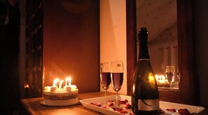 A table with a cake, two glasses of wine, a bottle of wine, and rose petals. - The Saffron Desert Camp (Sam)
