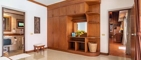 A spacious room with a large wooden wardrobe, a bench, and a small table with a vase of flowers.