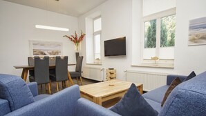 Un soggiorno moderno con un tavolino in legno, divani blu, un'area pranzo con sedie, un televisore a schermo piatto e una finestra vista alberi.