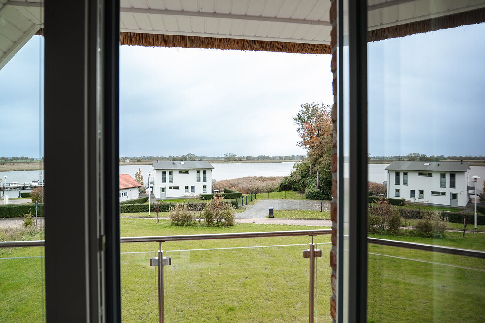 A view from a window overlooking a residential area with houses, a body of water, and a grassy field.