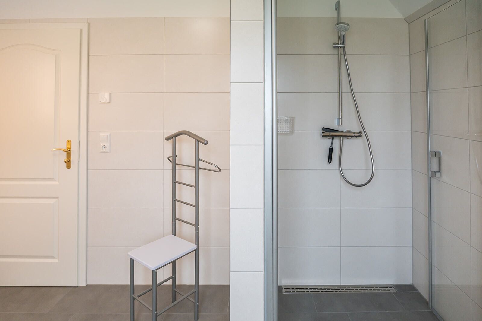 A bathroom with a shower, a toilet, and a small stool.