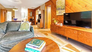 A modern living room with a sofa, coffee table, TV, and wooden panel walls. - Stylish Bungalow near Saugatuck (Fennville)