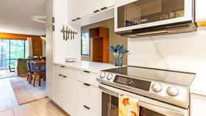 A modern kitchen with white cabinets, a stainless steel stove, and a microwave. - Stylish Bungalow near Saugatuck (Fennville)