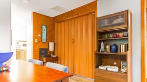 A room with a wooden-paneled wall, a wooden bookshelf with various items, a television, and a dining table with chairs. - Stylish Bungalow near Saugatuck (Fennville)
