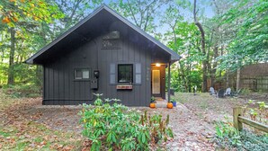 A small, dark wooden cabin with a sloped roof, a small porch with a bench, and a door with a window. - Stylish Bungalow near Saugatuck (Fennville)