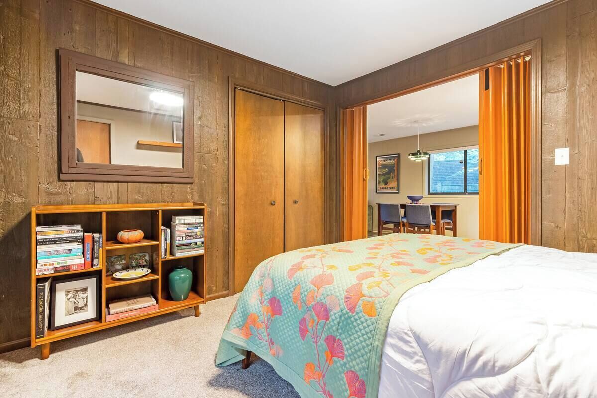 Ein Schlafzimmer mit einem Bett, einem Holzregal, einem Spiegel und einer Tür zu einem anderen Raum.