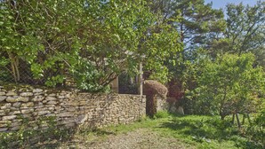 A stone wall with a rustic gate, surrounded by lush greenery and trees. - Lovely house with pool and garden (Saint-Léon-sur-Vézère)